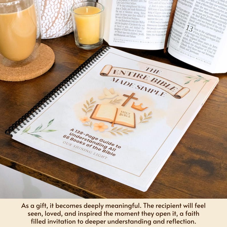 May include: A spiral-bound book titled "The Entire Bible Made Simple" with a floral and religious design. The cover features an open Bible, a cross, and a crown. The book is on a wooden surface, with a glass of coffee and a candle in the background.