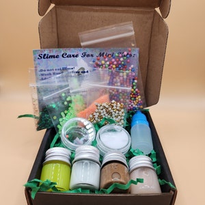 May include: A cardboard box containing slime-making materials. Inside are small jars of coloured slime, glitter, beads, and a bottle of activator. A card reads "Slime Care For Mini Kids".