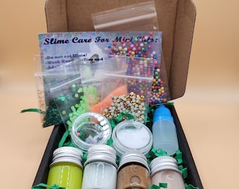 May include: An open cardboard box filled with slime-making supplies. The box contains small jars of colored slime, glitter, beads, and a bottle of activator. A card reads "Slime Care For Mini Kids".