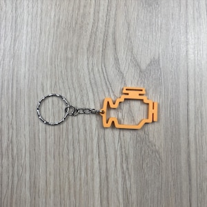 May include: Orange engine-shaped keyring with a silver key ring and chain. The keyring is a solid orange colour and features a detailed outline of an engine. The key ring and chain are made of silver-coloured metal.