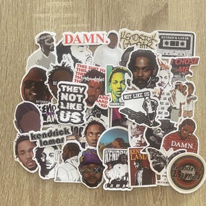 Op de afbeelding: Een verzameling kleurrijke stickers met de rapper Kendrick Lamar. De stickers bevatten verschillende afbeeldingen en tekst, waaronder "DAMN.", "Kendrick Lamar", "They Not Like Us" en "I Choose Me".