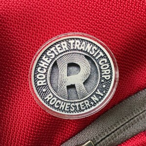 May include: A red backpack with a silver circular patch that says "Rochester Transit Corp." with a stylized "R" in the center.