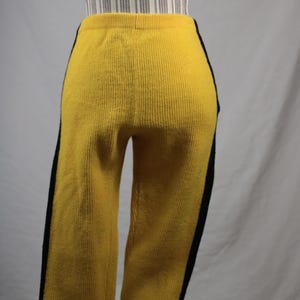 May include: Yellow knit pants with black side stripes. The pants have a ribbed texture and a high waist. The garment is displayed on a mannequin. The pants are a bright, solid color.
