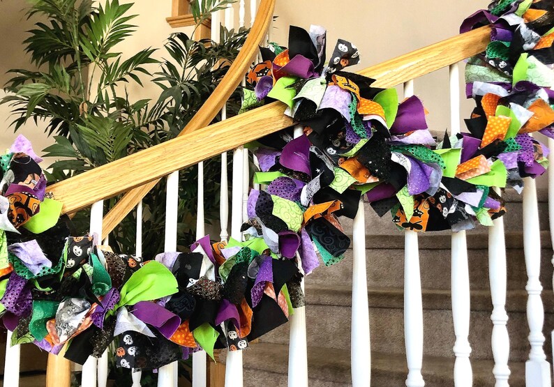 May include: A Halloween garland made of fabric scraps in black, green, orange, and purple. The garland is draped over a white banister and is decorated with various Halloween-themed patterns.