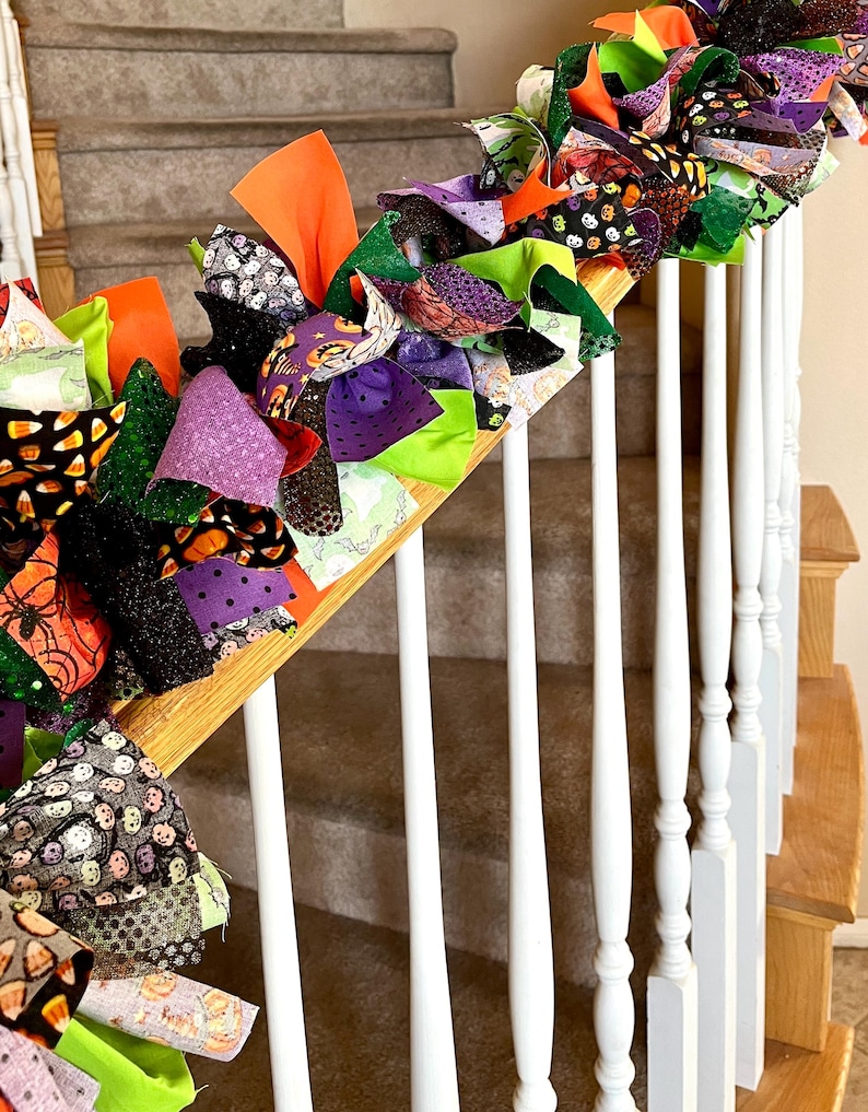 May include: A decorative fabric rag garland featuring a mix of orange, purple, green, and black fabric strips. The garland includes various patterns such as candy corn, pumpkins, spiders, and polka dots, tied together to create a textured display.