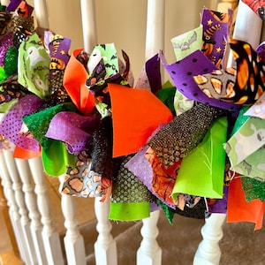 May include: A decorative garland made of tied fabric strips in various Halloween-themed patterns and colors, including ghosts, pumpkins, candy corn, bats, and solid orange, purple, lime green, and black glittery textures.