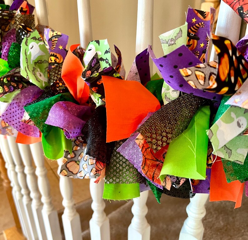 May include: A decorative garland made of tied fabric strips in various Halloween-themed patterns and colors, including ghosts, pumpkins, candy corn, bats, and solid orange, purple, lime green, and black glittery textures.