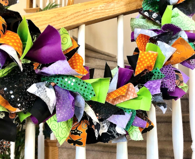 May include: A decorative rag wreath featuring a collection of fabric strips in vibrant shades of orange, lime green, purple, and black. The fabric pieces include various patterns such as polka dots, swirls, and Halloween-themed motifs.