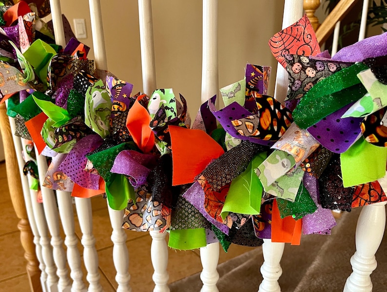 May include: A Halloween-themed rag garland featuring strips of fabric in orange, lime green, purple, and black. The fabric patterns include ghosts, pumpkins, candy corn, and spider webs, tied together to create a festive, textured decorative strand.