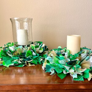 May include: Two green and gold fabric wreaths with candles in the center. The wreaths are made of fabric scraps and are a festive decoration for St. Patrick's Day.