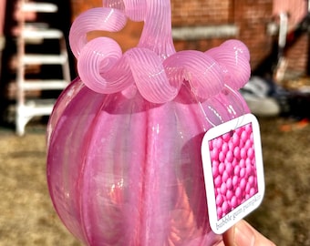 Può includere: Una zucca di vetro rosa con un design a spirale sul gambo. La zucca ha una finitura iridescente ed è etichettata "bubble gum pumpkin".