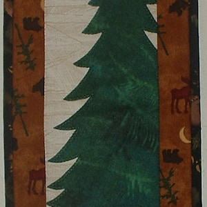 Può includere: Un arazzo da parete trapuntato marrone e beige con un albero verde e una silhouette di alce nera. Lo sfondo è di colore crema con una luna bianca e una stella gialla.