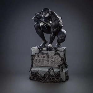 Puede incluir: Estatua en blanco y negro de Venom, un superhéroe de Marvel Comics, agachado sobre una lápida. La lápida dice "Here Lies Eddie Brock".