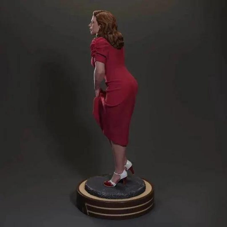 Puede incluir: Un vestido rojo con un corpi&ntilde;o ajustado y una falda fluida. El vestido lo lleva una mujer con el pelo rojo y est&aacute; de pie sobre una plataforma redonda.