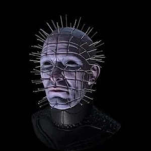 Könnte beinhalten: Nahaufnahme einer Person, die eine Maske mit einem Gitter aus Metallspitzen trägt. Die Maske ist aus Metall und hat ein Gittermuster. Das Gesicht der Person ist durch das Gitter sichtbar, und ihre Augen sind geschlossen. Die Maske ist dunkelgrau.