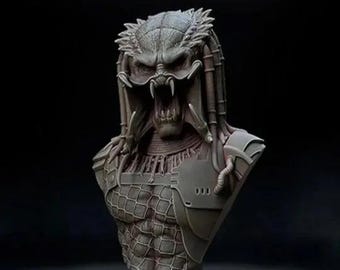 May include: A detailed bust sculpture of a Predator, a fictional alien hunter from the movie franchise. The sculpture is made of a gray, textured material and features a detailed head with a mask, sharp teeth, and dreadlocks. The Predator is wearing a detailed, textured armor with a net-like pattern.