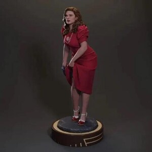 Puede incluir: Una figura de una mujer con un vestido rojo y tacones rojos. La figura est&aacute; de pie sobre una base redonda con un dise&ntilde;o marr&oacute;n y dorado.