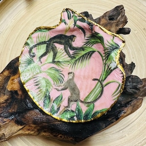 May include: A pink resin trinket dish with a gold rim, featuring a tropical leaf pattern and two monkeys.