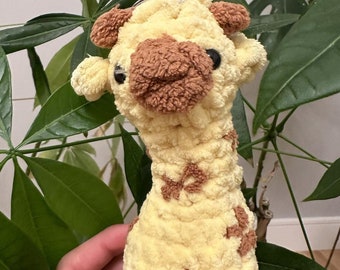 May include: A yellow and brown plush giraffe toy with a brown nose and black eyes. The giraffe is holding a silver ring in its mouth.