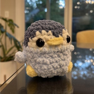 Puede incluir: Un pequeño juguete de peluche de pingüino de crochet azul y amarillo con ojos negros.