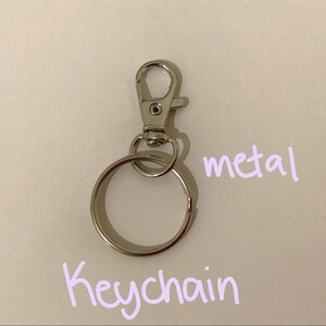 Puede incluir: Un llavero de metal plateado con un anillo redondo y un cierre de resorte.