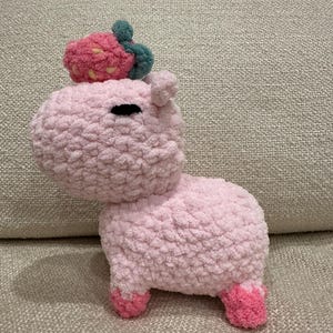Puede incluir: Un animal de peluche de crochet rosa con forma de hipopótamo con una fresa en la cabeza. La fresa también está hecha de crochet y tiene hojas verdes.