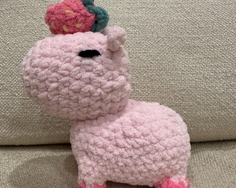 May include: A pink crocheted stuffed animal shaped like a hippopotamus with a strawberry on its head. The strawberry is also crocheted and has green leaves.