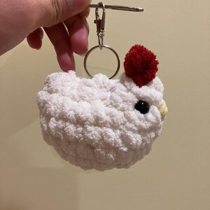 Puede incluir: Llavero de pollo blanco tejido a crochet con un pomp&oacute;n rojo en la cabeza. El llavero tiene un anillo de metal plateado y un cierre de metal plateado.