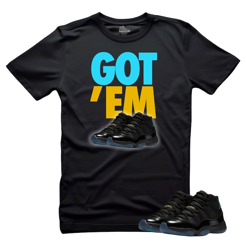 May include: Black t-shirt with the text "GOT 'EM" in blue and yellow. The shirt features an image of black and teal sneakers. The sneakers are also shown at the bottom of the shirt.
