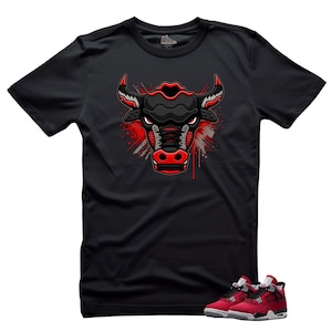 May include: Black t-shirt featuring a stylized bull head design in red, black, and gray. The bull graphic has a modern, geometric style. A pair of red and black sneakers with white soles are at the bottom of the image.