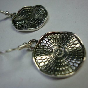 May include: A pair of silver earrings with a circular design. The earrings have a textured surface with a circular pattern.