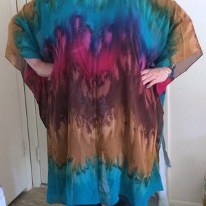 May include: A colorful, tie-dye tunic in shades of teal, brown, pink, and purple. The tunic has a loose, flowing fit with wide sleeves. The fabric appears to be lightweight and semi-sheer, suitable for warm weather.