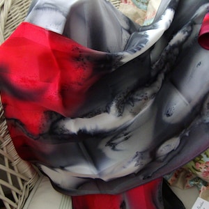 May include: A red, white and black silk scarf with a flowing, abstract design. The scarf is draped over a white wicker chair.