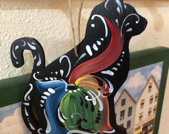 Pode incluir: Ornamento de gato de madeira preto com um design pintado de arco-íris. O gato está pendurado em uma corda e tem um contorno branco.