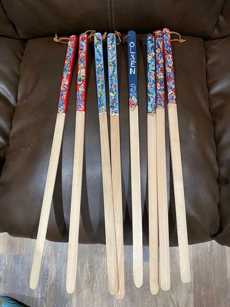 Op de afbeelding: Negen houten stokken met beschilderde ontwerpen. De stokken zijn versierd met bloemmotieven in rood, blauw en geel. E&eacute;n stok heeft de naam "OLSEN" erop geschilderd.
