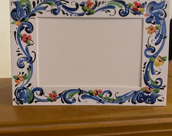 May include: A white picture frame with a blue, green, and orange floral design. The frame is made of cardboard and has a white mat.
