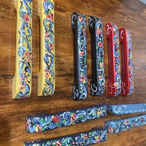 May include: A set of nine hand-painted wooden drawer pulls with floral designs. The pulls are in various colors, including yellow, blue, red, and black. The floral designs are intricate and detailed.