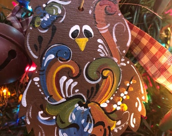 May include: A brown wooden owl ornament with painted details in shades of blue, green, yellow, and white. The owl has large eyes and a yellow beak.