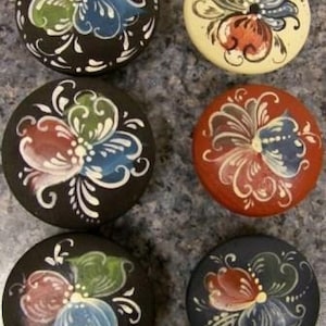 May include: Six round wooden boxes with painted butterfly designs. The boxes are painted in various colors, including black, white, red, blue, and green.