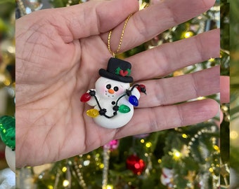 Snowman Ornament holding Christmas lights. Three dimensional, hand sculpted.