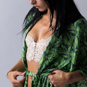 Puede incluir: Bata tipo kimono con estampado floral verde y azul marino con cintur&oacute;n a juego. La bata est&aacute; abierta, revelando un bralette de encaje blanco. Las mangas son largas y la bata est&aacute; atada a la cintura.