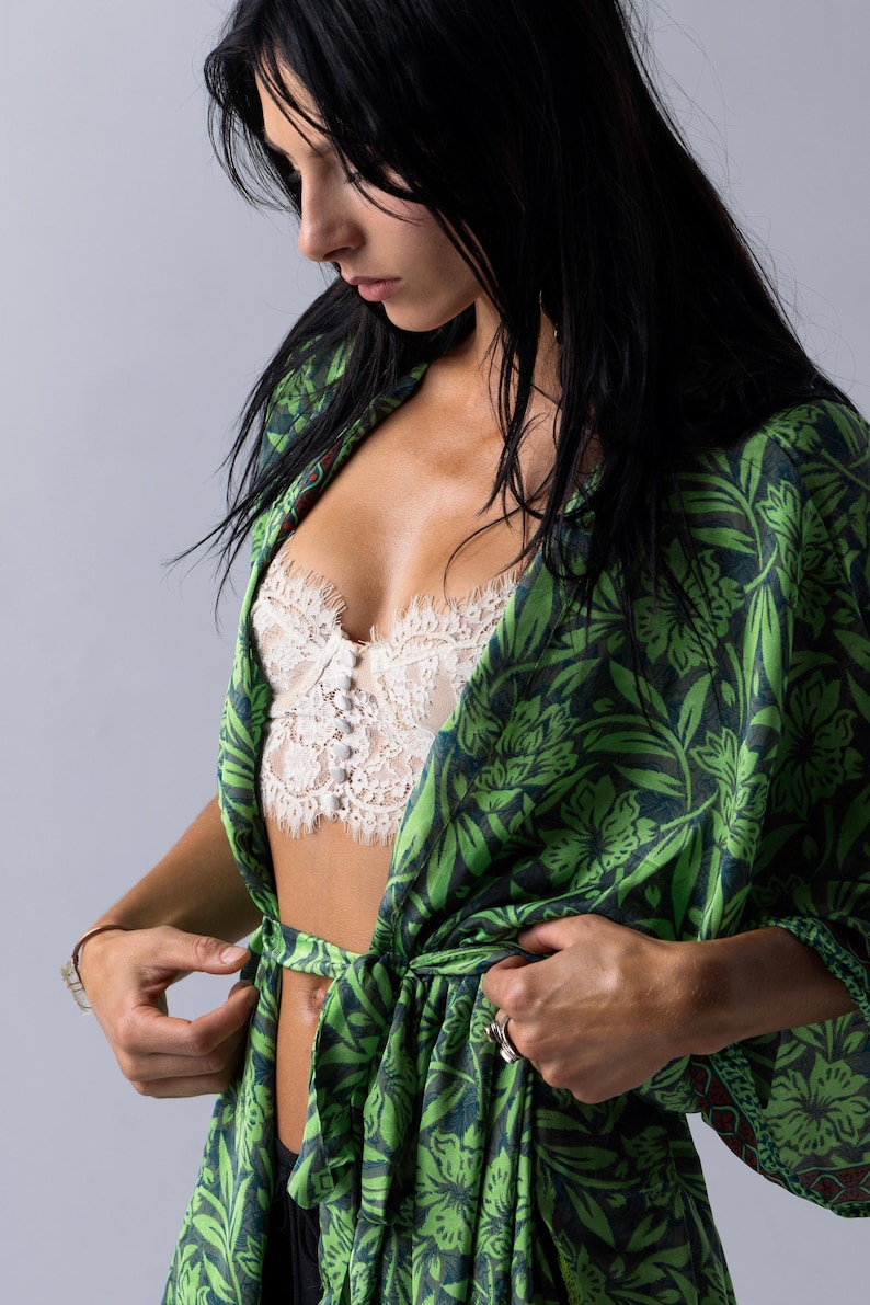 Puede incluir: Bata tipo kimono con estampado floral verde y azul marino con cintur&oacute;n a juego. La bata est&aacute; abierta, revelando un bralette de encaje blanco. Las mangas son largas y la bata est&aacute; atada a la cintura.