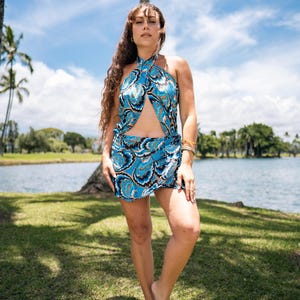 May include: A blue halter top and matching skirt set with a swirling white and black pattern. The outfit is worn outdoors near a lake with palm trees and a blue sky in the background. The skirt is mini-length.