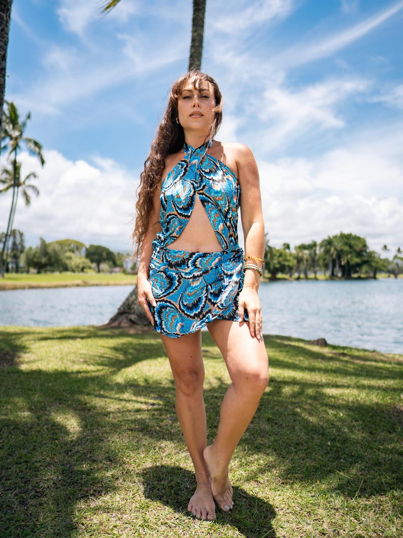 May include: A blue halter top and matching skirt set with a swirling white and black pattern. The outfit is worn outdoors near a lake with palm trees and a blue sky in the background. The skirt is mini-length.