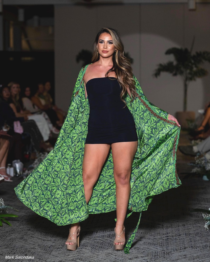 Puede incluir: Una mujer con un minivestido negro sin tirantes y un kimono largo verde con estampado de hojas. Lleva tacones de plataforma. La imagen est&aacute; tomada en un desfile de moda.