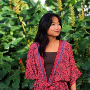 May include: A red and black floral print kimono-style robe featuring a dark brown tank top underneath. The robe has a tie-waist closure and a decorative blue and red patterned trim along the front opening and neckline, with wide sleeves.