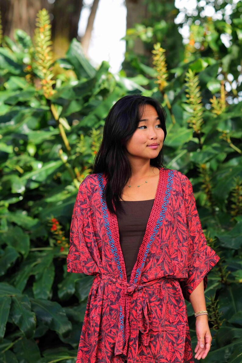 May include: A red and black floral print kimono-style robe featuring a dark brown tank top underneath. The robe has a tie-waist closure and a decorative blue and red patterned trim along the front opening and neckline, with wide sleeves.