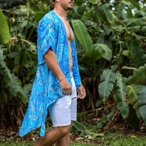 May include: A bright blue open-front kimono featuring a detailed silver paisley pattern, paired with plain white shorts. The lightweight garment has short sleeves and a loose, flowing fit that extends to the mid-thigh, worn over bare skin.