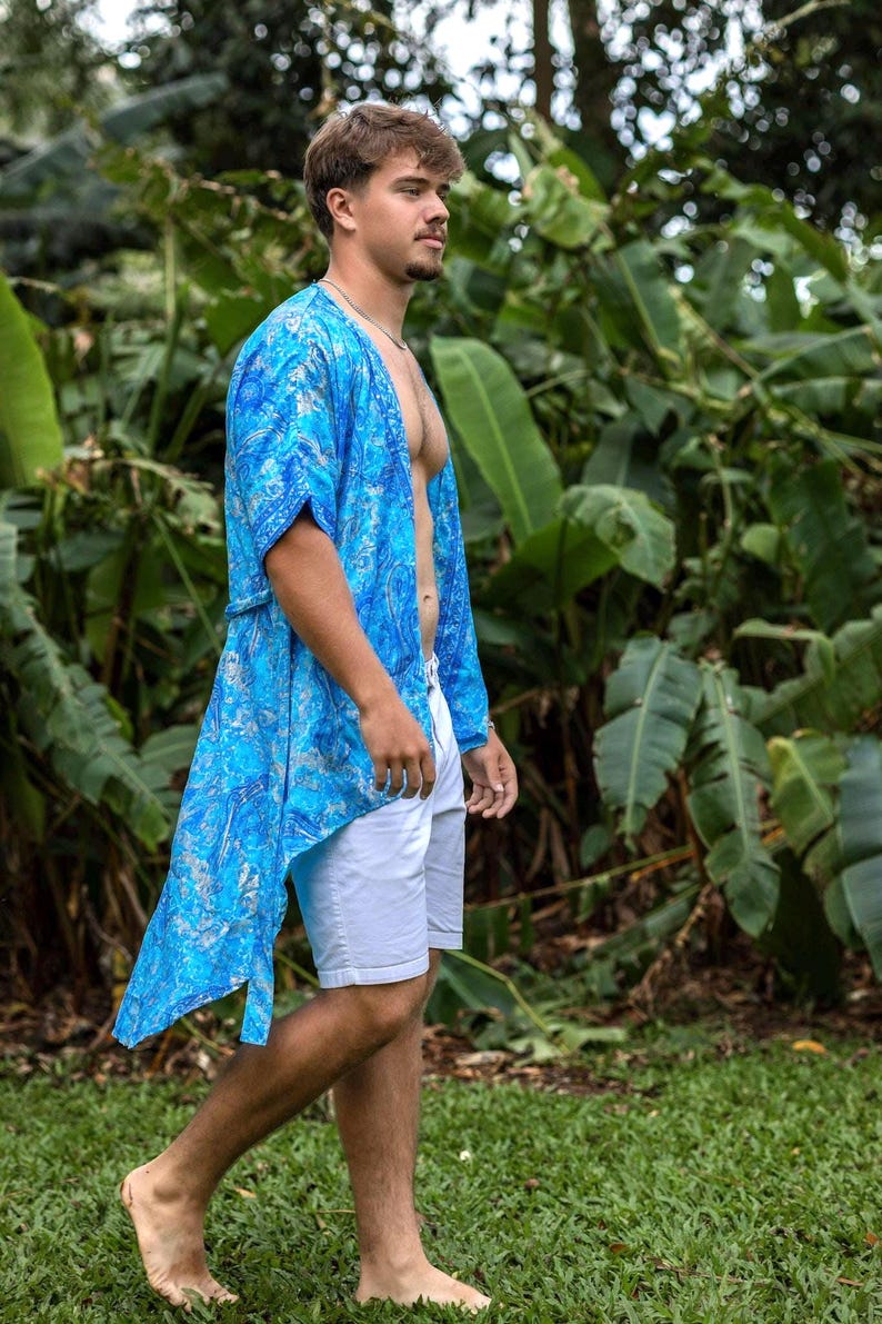 May include: A bright blue open-front kimono featuring a detailed silver paisley pattern, paired with plain white shorts. The lightweight garment has short sleeves and a loose, flowing fit that extends to the mid-thigh, worn over bare skin.
