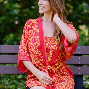 May include: A vibrant red and yellow floral print robe and matching top. The robe has a contrasting red trim and is tied at the waist. The outfit is made of a lightweight fabric, perfect for lounging.